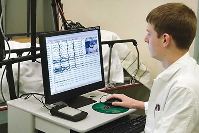 Étudiant consultant un moniteur afin d'analyser les signaux électriques émis par les systèmes nerveux d'un patient allongé sur un lit.