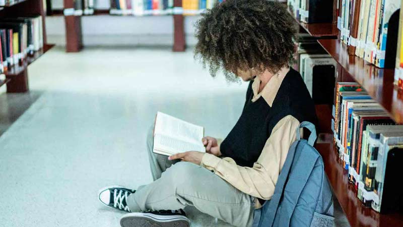 Jeune homme étudiant assis par terre à la bibliothèque