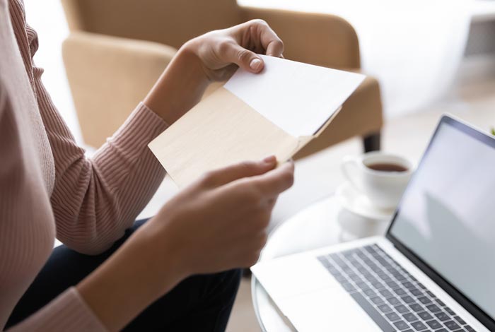 Une personne prenant place devant son ordinateur portable ouvre une enveloppe.