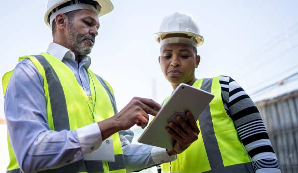 Un homme et une femme consultent des documents à l'aide d'une tablette sur un chantier.