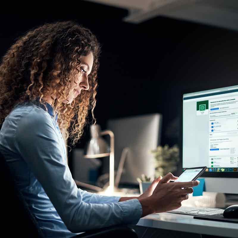 Une étudiante est assise à un bureau devant un ordinateur et un téléphone intelligent.