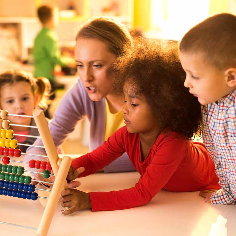 Une éducatrice dirige une activité avec trois enfants prenant place autour d'une table. 