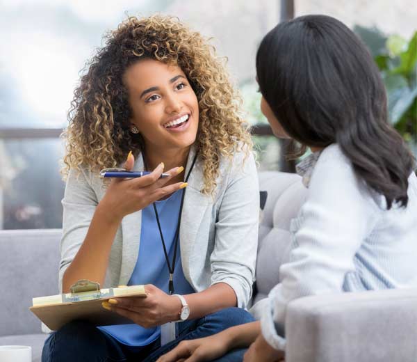 Une jeune avocate positive fait des gestes lorsqu'elle parle avec une cliente. Elle sourit chaleureusement en discutant avec la jeune femme.