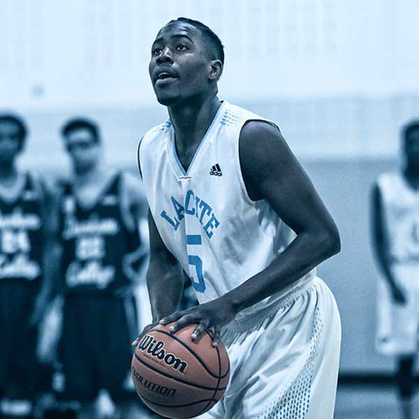 Un joueur de basket en maillot blanc, portant le numéro 5, se prépare à tirer un lancer franc. D’autres joueurs, en arrière-plan, semblent observer la scène. L’image met l’accent sur sa concentration et son geste.